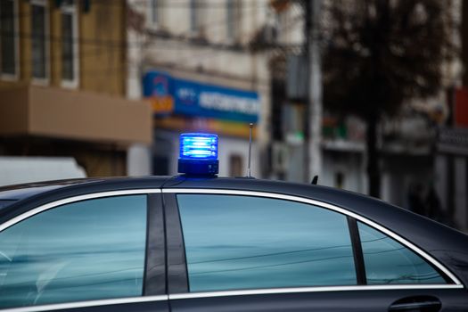 blue flashing light on top of black government car on daytime city street.