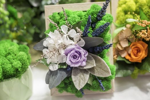 Decorative floristic arrangement of artificial flowers and stabilized moss, soft focus, selective focus.