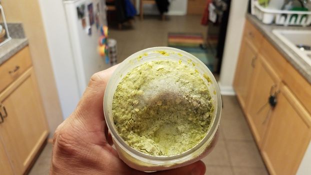 hand holding container of green pesto sauce with ice crystals in kitchen