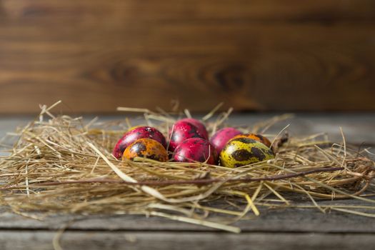 Painted easter eggs in a makeshift straw nest on a wooden background. Easter background