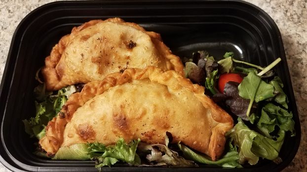 Puerto Rican fried beef turnover and salad in container on counter