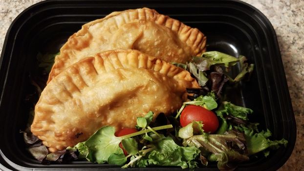 Puerto Rican fried beef turnover and salad in container on counter