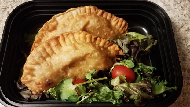 Puerto Rican fried beef turnover and salad in container on counter