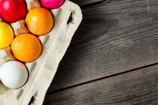 Dyed easter eggs in cardboard box on wooden background. Easter background with space for a text.