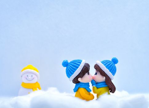 Tourism and travel concept: Miniature people kissing each other in winter snow with little snowman in the background