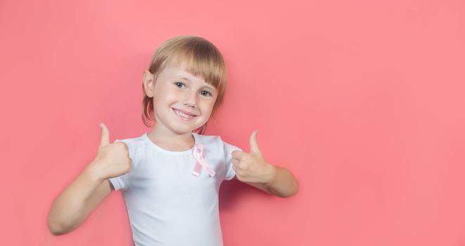 .Little girl showing two thumbs up in white t-shirt and with pink breast cancer awareness ribbon