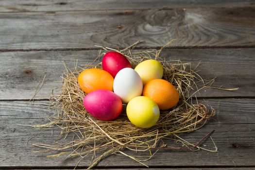 Painted easter eggs in a makeshift straw nest on a wooden background. Easter background