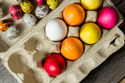 Dyed easter eggs in cardboard box on wooden background. Easter background