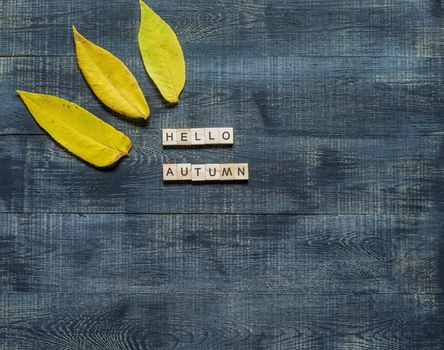 Text hello autumn framed by autumn fallen leaves on a dark wooden background.