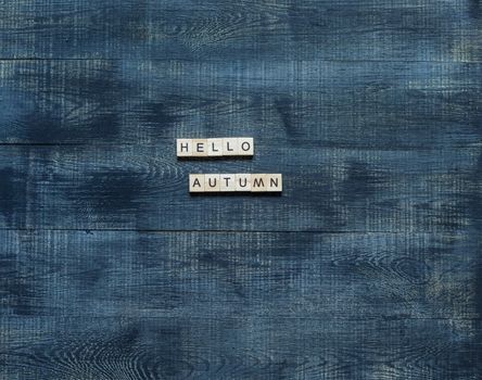 the inscription "hello autumn" on wooden dice on a wooden background.
