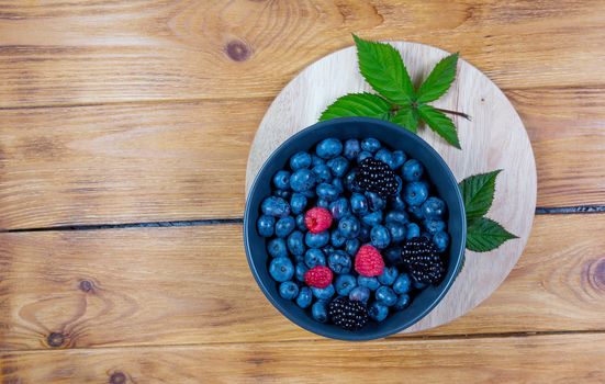 blueberry berry in dark gray ceramic bowl on wooden cutting board on dark blue wooden background. top view