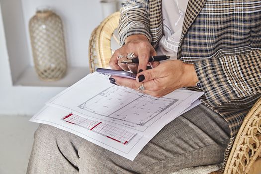 Woman interior designer with interior plans for a new project holds a mobile phone in her hands, freelancer talks with a customer. Soft socus