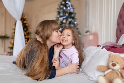 Little girl spends time playing with mom while lying in bed. Christmas tale. Happy childhood.