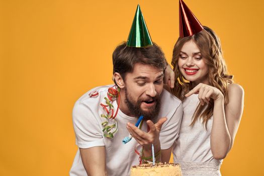 Happy man and woman in a cap celebrating a birthday on a yellow background with a cake in their hands. High quality photo