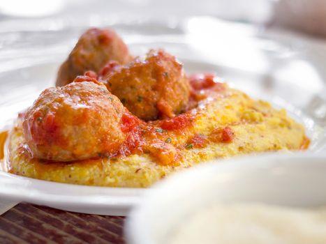 Polenta with meatballs in tomato sauce. Traditional italian pork and beef meatballs served on polenta with tomato sauce, basil, parmesan and a drizzle of olive oil.