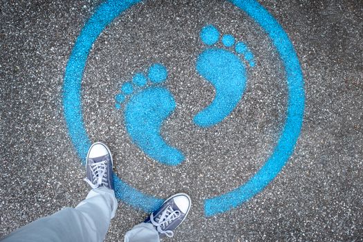 Man standing on blue dot. Sign painted on the pavement reminding users to maintain a physical distance of 3 feet / 1 meter during the COVID-19 pandemic.