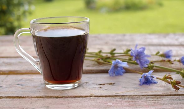 Close-up chicory drink on the wooden table in the garden at summer day. A bouquet of calendula flowers on the table. Herbal medicine concept