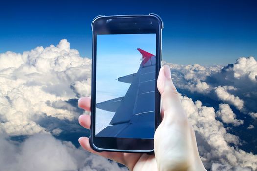 Travelling in a plane in the sky. Composing of a female hand holding a smartphone taking a picture