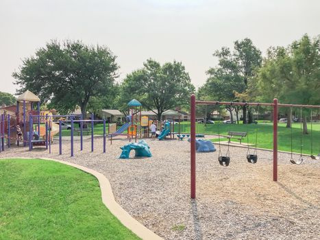 Swing set at large playground in residential neighborhood near Dallas, Texas, America. Community park with row of single family houses in background