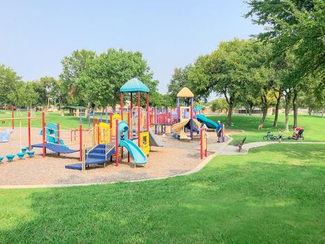 Colorful playground near residential neighborhood in Richardson, Texas, America. Community facility surrounded by large oak trees and green grass lawn