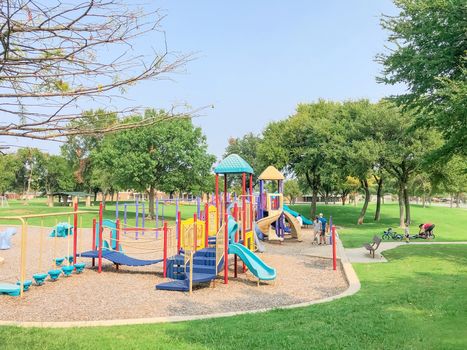 Colorful playground near residential neighborhood in Richardson, Texas, America. Community facility surrounded by large oak trees and green grass lawn