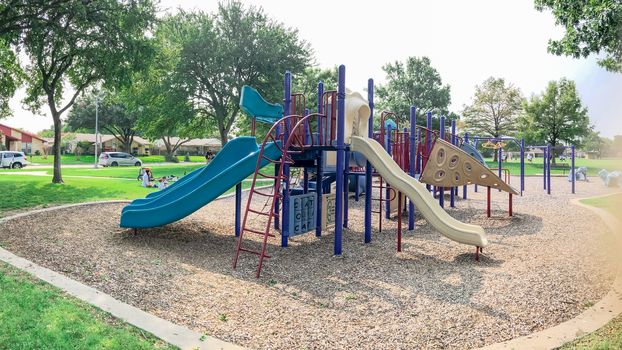 Variety of slide and swing at Colorful playground near residential neighborhood in Richardson, Texas, America. Community facility surrounded by large oak trees and green grass lawn