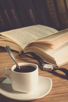 An open book and a cup of coffee on the table. Reading a book in a cafe. Stylish photo of the coffee house. A cup of coffee in the evening light. Watch with leather strap
