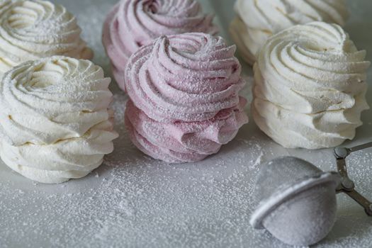 Sweet dessert. White and pink marshmallows lying on the table in powdered sugar. Close-up.
