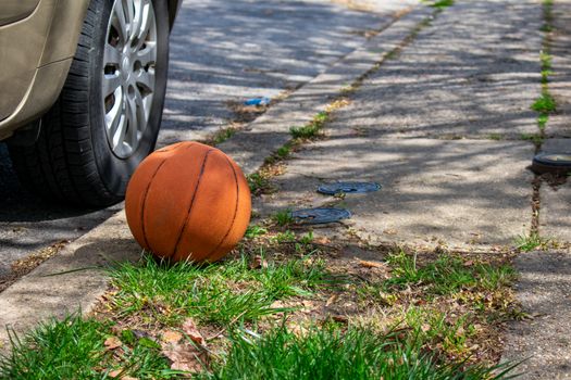 A Forgotten Orange Basketball Next to a Car on a Suburban Street