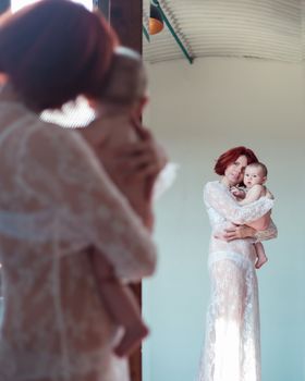 Mom holds the baby in her arms while standing in front of the mirror