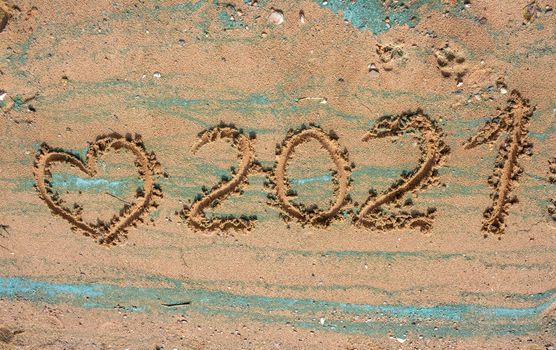 The concept of a New year. Heart and numbers 2021 in the sand. Summer beach holidays . The message is handwritten.