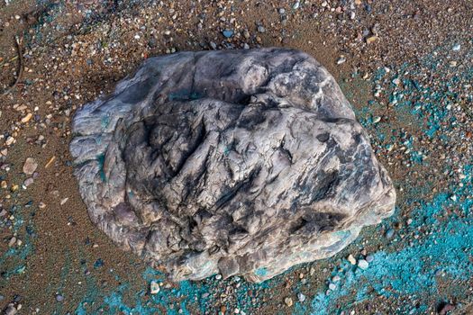 The stone lies in the sand on the coast.Nearby is a turquoise strip of river foam from the fuel.The concept of the environment.