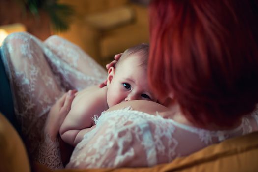 Mother in white dress breastfeeding cute baby boy with child looking at camera