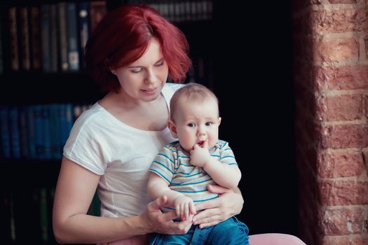 Young pretty woman holding a 6 months old baby in her arms, the baby stuck his fingers in his mouth