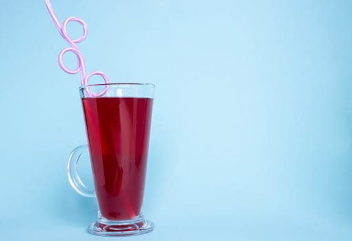 A glass with strawberry juice and a curved tube on a blue background. Space for your text.