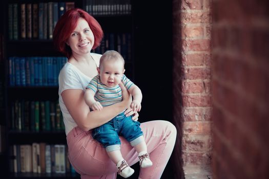 Young pretty woman holding a 6 months old baby in her arms, mother and baby smiling at the camera