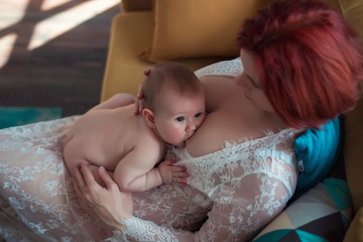 Mother in white dress breastfeeding cute baby boy with child looking at camera
