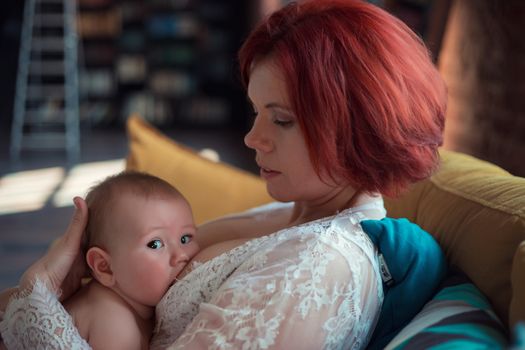 Mother in white dress breastfeeding cute baby boy with child looking at camera