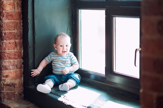 Little baby biy sits on the windowsill and smiles with all his mouth