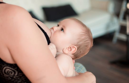 A young mother is breastfeeding her little child and looking at him tenderly