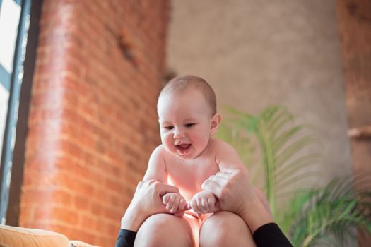 The baby lies on the lap of the mother in the airplane pose, the mother plays with the baby