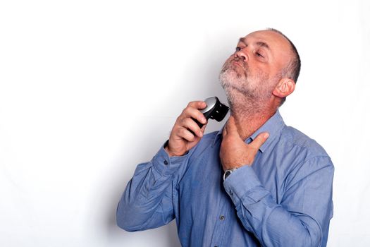 Portrait of man shaving his beard with electric shaver against white background
