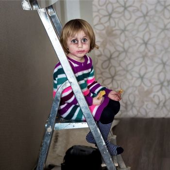Cheerful little girl having fun sits on a stepladder and smiles