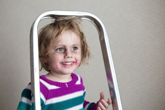 Cheerful little girl having fun sits on a stepladder and smiles