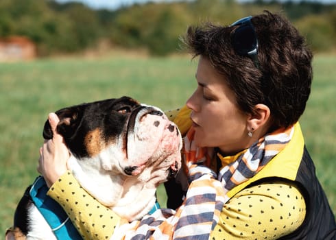 a woman and an English bulldog hugging in a clearing on a warm summer day