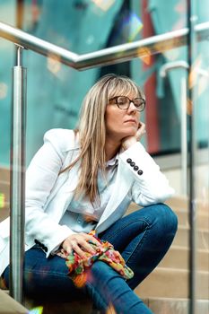 portrait of a woman in glasses sitting on the stairs in city centre