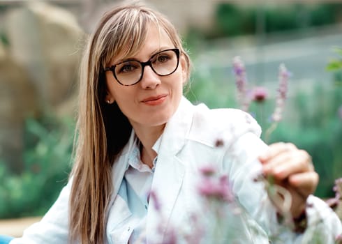portrait of a woman in glasses and white coat looking at flowers
