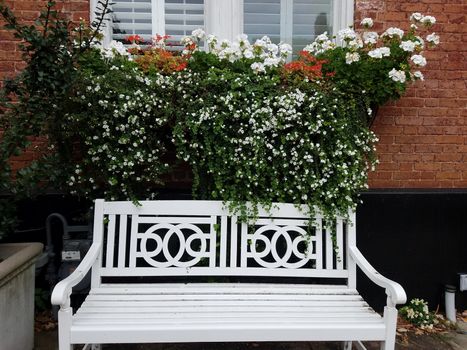 white bench with red brick house and white flowers