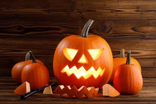 Carving of Halloween pumpkins in progress, pieces and cutting knife on wooden background, lantern is glowing