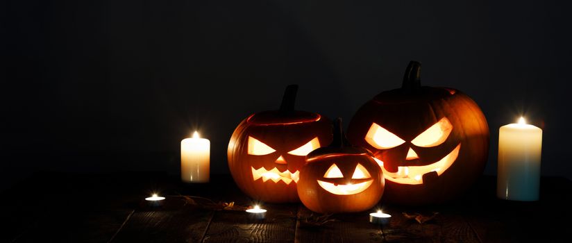 Halloween pumpkin head lanterns and burning candles on black background